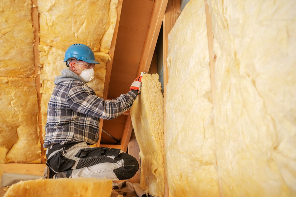 Worker installing new insulation in residential attic after rodent damage cleanup